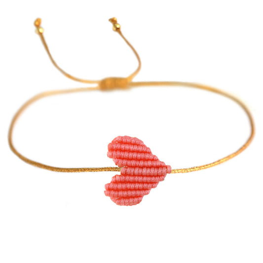 Armband mit goldenem Band und geflochtenem Herz in koralle von Love biza. Dank praktischem Schiebeknoten passt das Armband an jedes Handgelenk! 