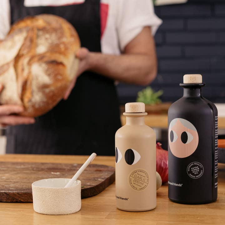 200 ml Natives Olivenöl mit Knoblauch von YiaYia & Friends - Produktabbildung in Küche mit Brot & Salz sowie Olivenöl pur