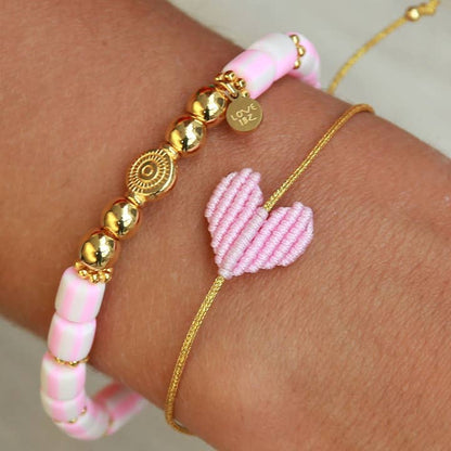 Armband mit goldenem Band und geflochtenem Herz in rosa von Love Ibiza. Dank praktischem Schiebeknoten passt das Armband an jedes Handgelenk! 
